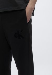 Μαύρο φούτερ παντελόνι με μαλακή υφή, διαθέτει ανάγλυφο, τονικό λογότυπο "cK" στην αριστερή πλευρά και εσοχή τσέπης στη δεξιά.