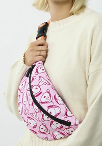 Borsa a tracolla in tessuto rosa con stampe di animali dei cartoni animati, cerniera nera e tracolla regolabile a righe arancioni. Texture morbida e forma incassata.