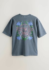 Graues T-Shirt mit kurzen Ärmeln, auf dem hinten der Schriftzug „Fleetwood Mac“ und ein kreisförmiges Blumenmuster mit blauen und grünen Blumen zu sehen sind.