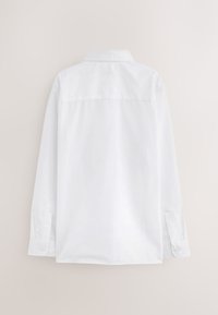 Vue arrière d'une chemise blanche unie à manches longues avec poignets boutonnés et col classique sur un fond neutre.