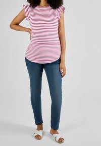 Różowo-biała bluzka w paski z falbanowymi rękawami, zestawiona z niebieskimi, dopasowanymi dżinsami i białymi sandałami z krzyżującymi się paskami. Gładka faktura i swobodny krój.