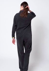 Czarny sztruksowy kombinezon z długimi rękawami, o luźnym kroju i elastycznym pasie, z bocznymi kieszeniami i detalem z tyłu.