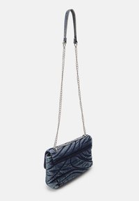 Borsa a spalla in denim con un motivo trapuntato, manico ad anello superiore e tracolla in catena argentata. Colore blu con variazioni di texture.