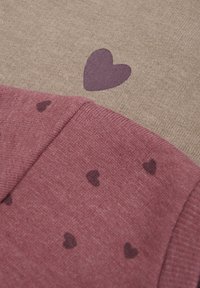 Rosa tyg med små mörka hjärtan, lager på lager över beige tyg med ett större mörkt hjärta. Mjuka, strukturerade stickade material.