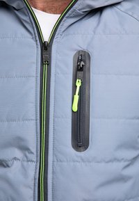 Jasnoniebieska kurtka puchowa z zamkiem błyskawicznym z przodu, z kontrastowym czarnym zamkiem i jasnoczerwonym uchwytem. Teksturowany materiał z pikowanym wzorem.