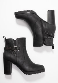 Botas negras hasta el tobillo hechas de cuero sintético, con cremalleras laterales, una correa texturizada con acentos metálicos y un tacón grueso.
