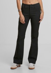 Rozšířené černé kalhoty s vertikálními pruhy, s přiléhavým pasem a jemnou texturou. V kombinaci s bílými teniskami pro neformální vzhled.