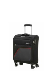 Valise noire à texture en tissu, avec un accent rouge, quatre roues, une poignée rétractable et une poche avant zippée.