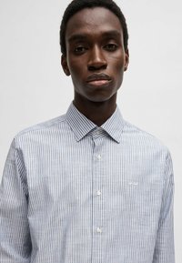 Lichtblauw en wit gestreept shirt met een button-down kraag, zichtbare knopen aan de voorkant en een klein logo op de linkerkant van de borst. Katoenen stoftextuur.