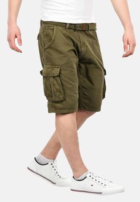 Grüne Cargo-Shorts mit mehreren Taschen und flachem Bund. Tragen sie mit weißen Sneakers, die ein Mesh-Design und rote Akzente aufweisen.
