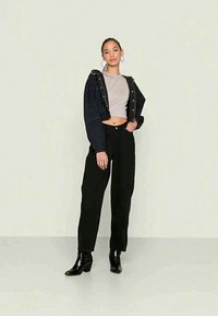 Casaco preto curto com detalhamentos prateados, top cinza curto, calças pretas de cintura alta e botas de salto pretas contra um fundo claro.