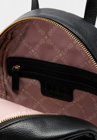 Zwart leren rugzak interieur met een lichtroze voering. Beschikt over een ritsvak en een merklogo dat is ingebed in de zwarte stof. Gouden ritsdetails.