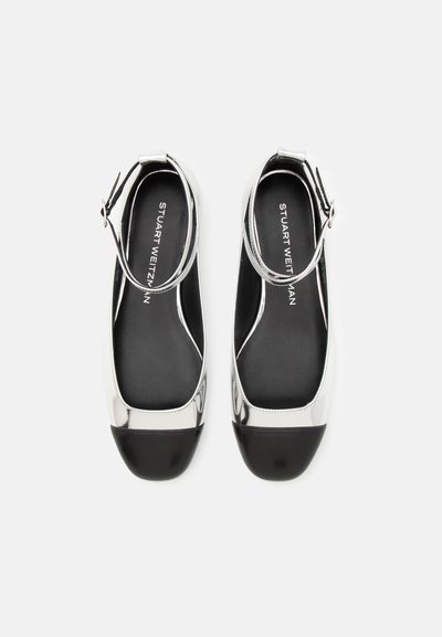 Silberne Lacklederflats mit schwarzen Zehenkappen und Knöchelriemen, die ein rundes Zehendesign und eine glatte, glänzende Oberfläche aufweisen.