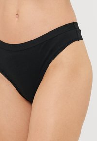 Sorte bikini-bunn laget av myk stoff, med en jevn midje og minimal dekning design for komfort og enkel påkledning.