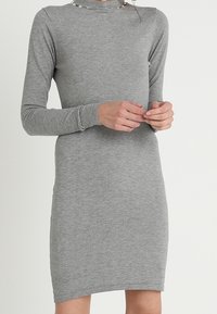 Abito grigio a maniche lunghe con collo alto. Realizzato in morbido tessuto elasticizzato, dalla silhouette aderente e dalla texture liscia.