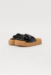 Sandales noires à enfiler avec une semelle en liège texturée, présentant une bride supérieure tressée et un design à bout ouvert. Fini en cuir lisse.