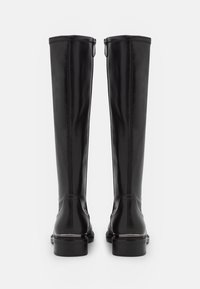 Czarne skórzane kozaki sięgające do kolan o gładkiej teksturze, kontrastowe przeszycia oraz zamek błyskawiczny z boku dla łatwego zakładania. Niska, klepana pięta.
