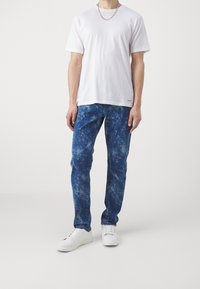 Bílé tričko s krátkými rukávy spojené s modrými džíny s batikováním a bílými teniskami. Oblečení má uvolněný střih a ležérní design.