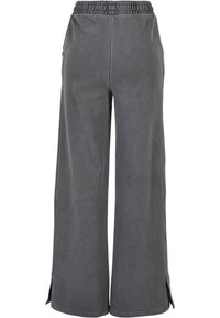 Pantalon gris à jambes larges en tissu doux avec une ceinture élastique et des poches latérales, présentant des coutures discrètes et des fentes latérales à l'ourlet.