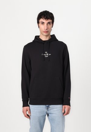 Juodas hoodie su kengūros kišene, raišteliais ir balta siuvinėtą logotipu. Minkšta medžiaga, kasdieniškas kirpimas, su šonu su įsiūtomis apykaklėmis ir juosmeniu.