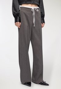 Szerokie szare spodnie z fakturowanej tkaniny, z elastycznym paskiem związywanym na sznurek i kontrastowym białym krawatem, zestawione z czarnymi, spiczastymi butami.