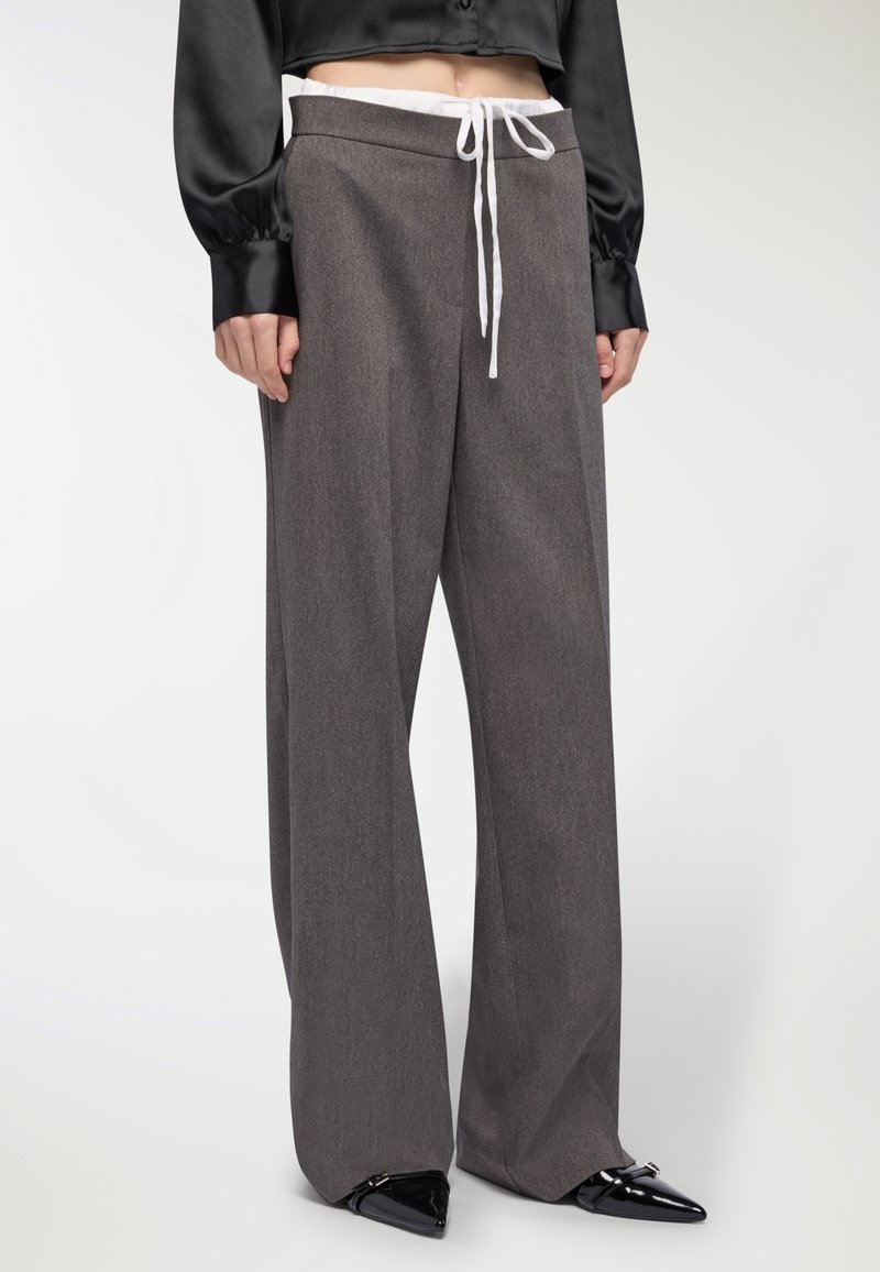 Szerokie szare spodnie z fakturowanej tkaniny, z elastycznym paskiem związywanym na sznurek i kontrastowym białym krawatem, zestawione z czarnymi, spiczastymi butami.