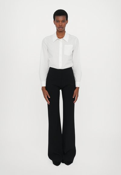 Witte button-up overhemd met een kraag en een enkele borstzak, gecombineerd met hoogwaisted zwarte flared pantalons, wat een scherpe silhoët creëert.