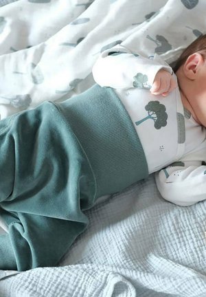 Tenue pour bébé comprenant une chemise blanche à manches longues avec des motifs d'arbres, associée à un pantalon doux teal et une taille côtelée, reposant sur une couverture texturée.