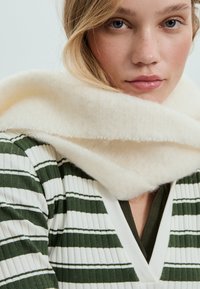 Groen-wit gestreepte trui met een geribbelde textuur, gecombineerd met een zachte, crèmekleurige sjaal met een fleeceachtige afwerking en opgerolde randen.