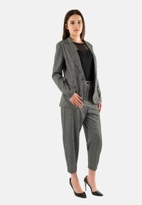 Traje a rayas grises con chaqueta entallada y pantalones ajustados, combinado con una blusa negra y zapatos de tacón negro. Textura suave.