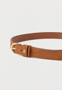 Tan leather belt with a gold-tone buckle and embossed logo. Smooth texture with a classic design, featuring a single prong closure.