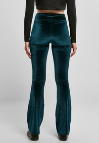 Baršunaste hlače sa širokim nogavicama u tamno tirkiznoj boji, s visokim strukom i glatkom teksturom. Istaknute su suptilnim sjajem i čistim detaljima šavova.