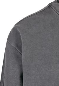 Tejido de sudadera gris acanalado con una superficie texturizada. El diseño cuenta con un cuello redondo y un ajuste holgado, enfatizando la simplicidad.