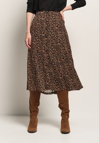 Jupe midi en imprimé léopard marron et noir avec un design fluide, dotée d'une taille haute et d'un tissu léger. Associée à des bottes en daim marron.