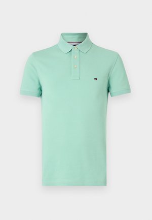 Polo de color verde claro hecho de algodón, con cuello, tres botones y un pequeño logo en el pecho izquierdo. Mangas cortas, textura suave.