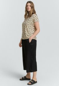 Majica kratkih rukava krem boje s crnim cik-cak uzorkom, uparena s crnim culottes i ravnim crnim sandalama. Outfit ima udoban kroj.