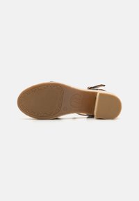 Suela de sandalia de cuero marrón con agarre de goma texturizado, que presenta un logo elevado y un diseño de tracción floral para mayor estabilidad.