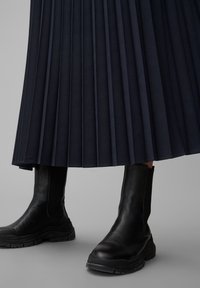 Navy pleated skirt with a flowing texture, paired with black leather ankle boots featuring a chunky sole and smooth finish.