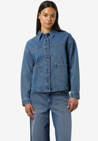 Chaqueta de mezclilla azul con cuello puntiagudo, frontales con botones y dos bolsillos delanteros. Presenta un corte relajado y una textura de peso medio.