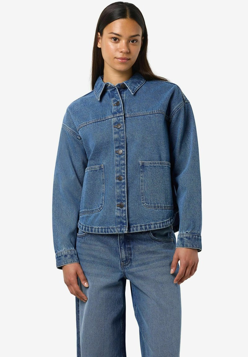 Chaqueta de mezclilla azul con cuello puntiagudo, frontales con botones y dos bolsillos delanteros. Presenta un corte relajado y una textura de peso medio.