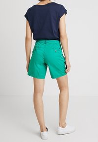 Pantalones cortos de algodón verdes con un ajuste relajado, que cuentan con bolsillos traseros y una textura suave, combinados con una camiseta sin mangas de color azul marino.
