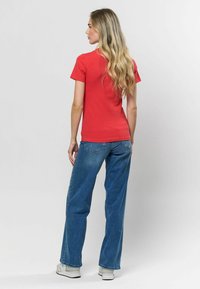 Raudona dryžuota trumpomis rankovėmis marškinėlius derinami su mėlynomis plačiomis kelnėmis. Modelis dėvi baltus sportbačius. Lygus audinys, laisvas modelis.