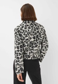 Luipaardprint jas van zacht fabric, met een hoge kraag en lange mouwen. Grijs en zwart patroon op een lichte achtergrond.