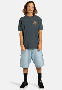 Dunkelgraues Baumwoll-T-Shirt mit einem bunten Grafikdesign auf der Brust, kombiniert mit hellblauen Denim-Shorts, schwarzen Sneakers und schwarzen kniehohen Socken.