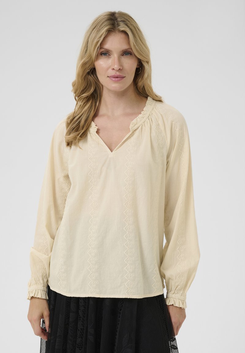 Cremfarbige Bluse mit langen Ärmeln, V-Ausschnitt und strukturierten Stickdetails vorne und an den Bündchen. Weicher, leichter Stoff.
