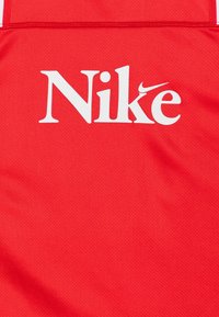Czerwony sportowy materiał z białym stylizowanym napisem "Nike" i małym logo Nike wkomponowanym w literę "k".