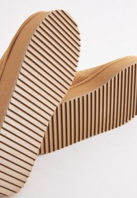 Gros plan des semelles de chaussures beiges avec des rainures horizontales profondes pour une bonne adhérence sur chaque semelle.