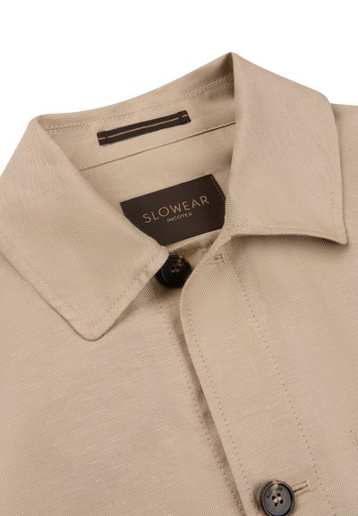 Camisa beige con cuello y botones negros, con etiqueta "SLOWEAR INCOTEX" dentro del cuello.