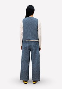 Gestreepte blauw-witte top gecombineerd met bijpassende wijde broek; textuurstof. Achteraanzicht toont twee achterzakken en casual schoenen.