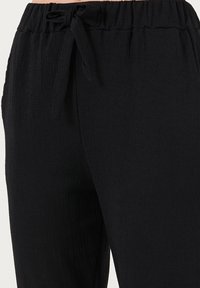 Zwarte, geplooide stoffen broek met een trekkoord in de taille. De textuur lijkt licht van gewicht en heeft een lichte structuur, geschikt voor casual kleding.